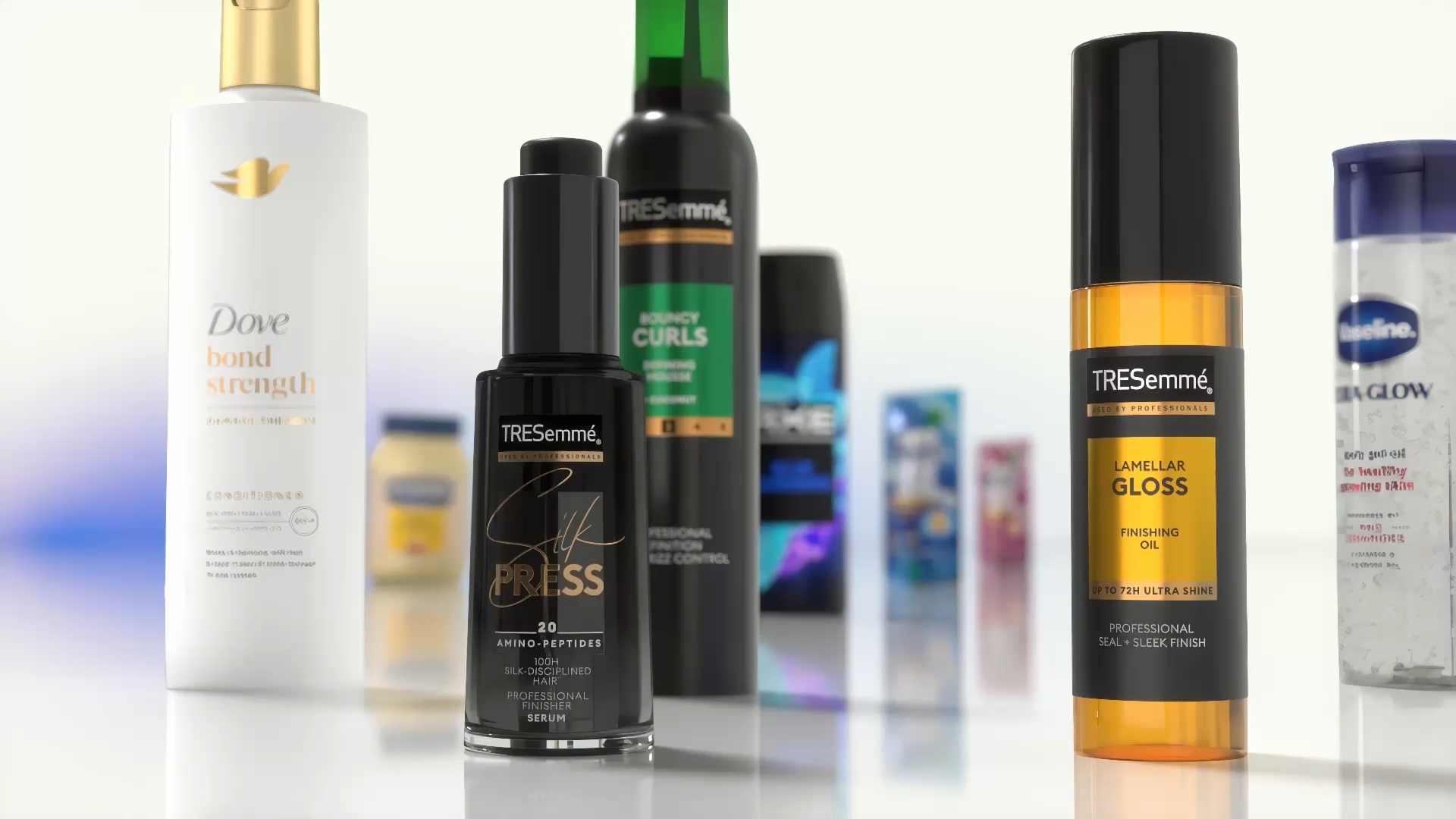 Nahaufnahme verschiedener Haar- und Körperpflegeprodukte auf einer reflektierenden Oberfläche. Zu sehen sind unter anderem Dove Bond Strength Conditioner, TRESemmé Silk Press Serum, TRESemmé Lamellar Gloss Finishing Oil und weitere Unilever-Produkte im Hintergrund.